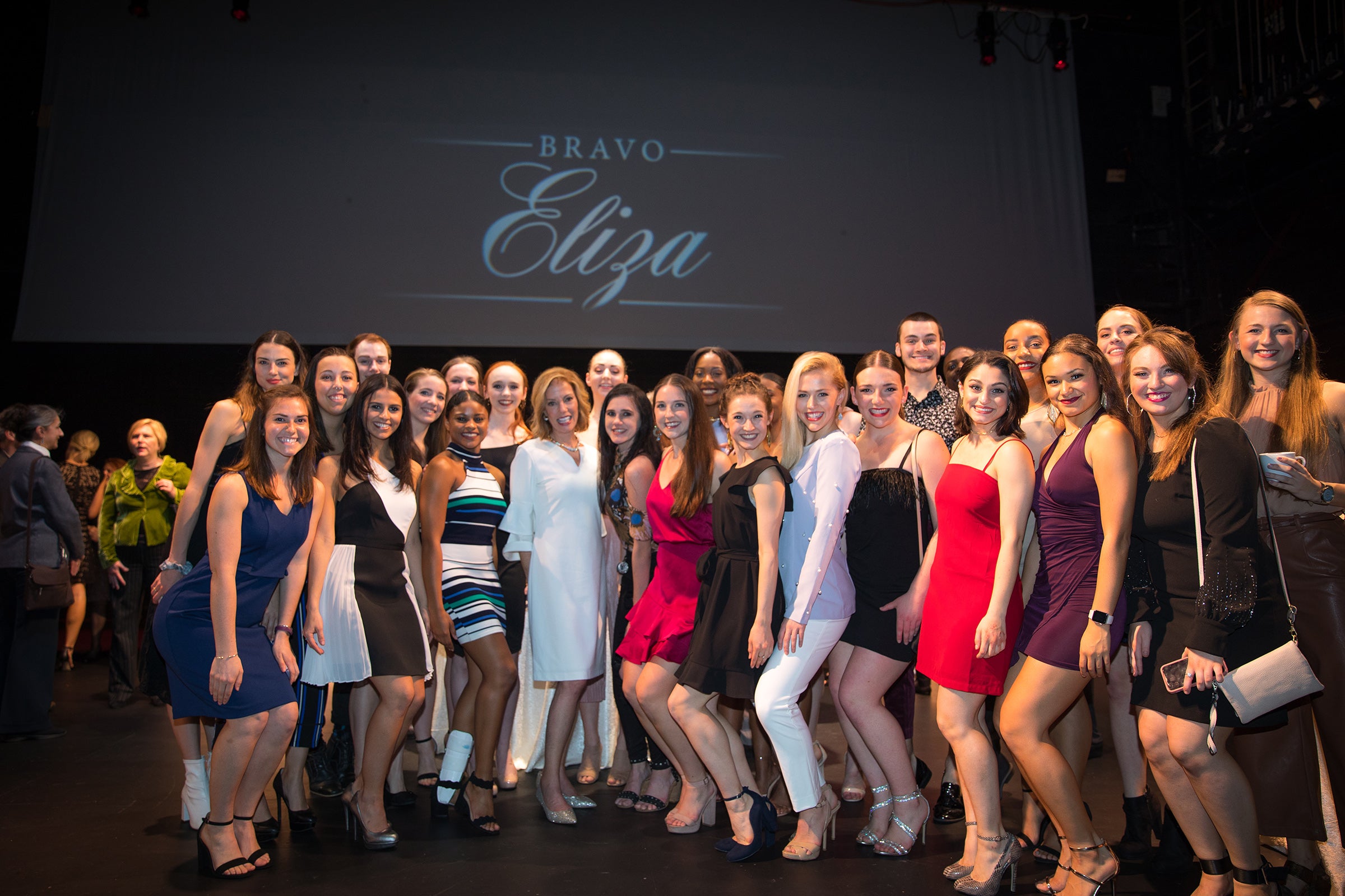 A group of women stand on a stage and pose for a photo