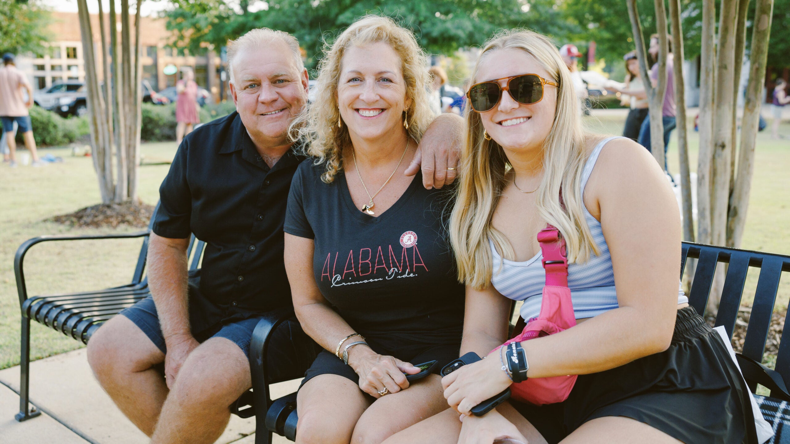 A family of three poses for a photo on a park bench.