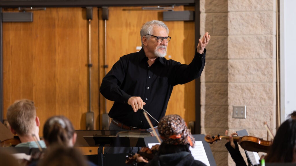 A white male conducts an orchestra