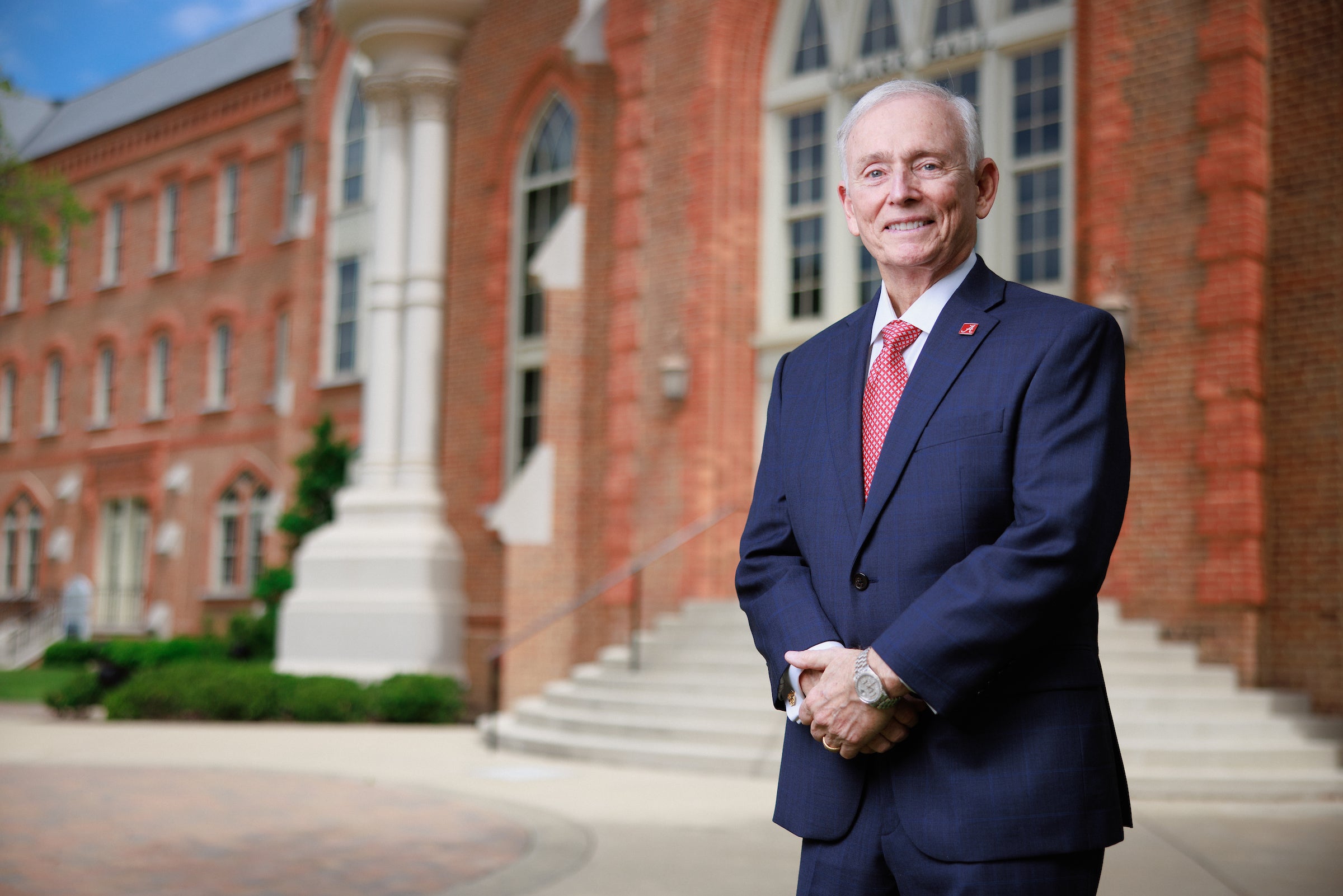 A man poses for a picture while standing in front of a brick building on a college campus
