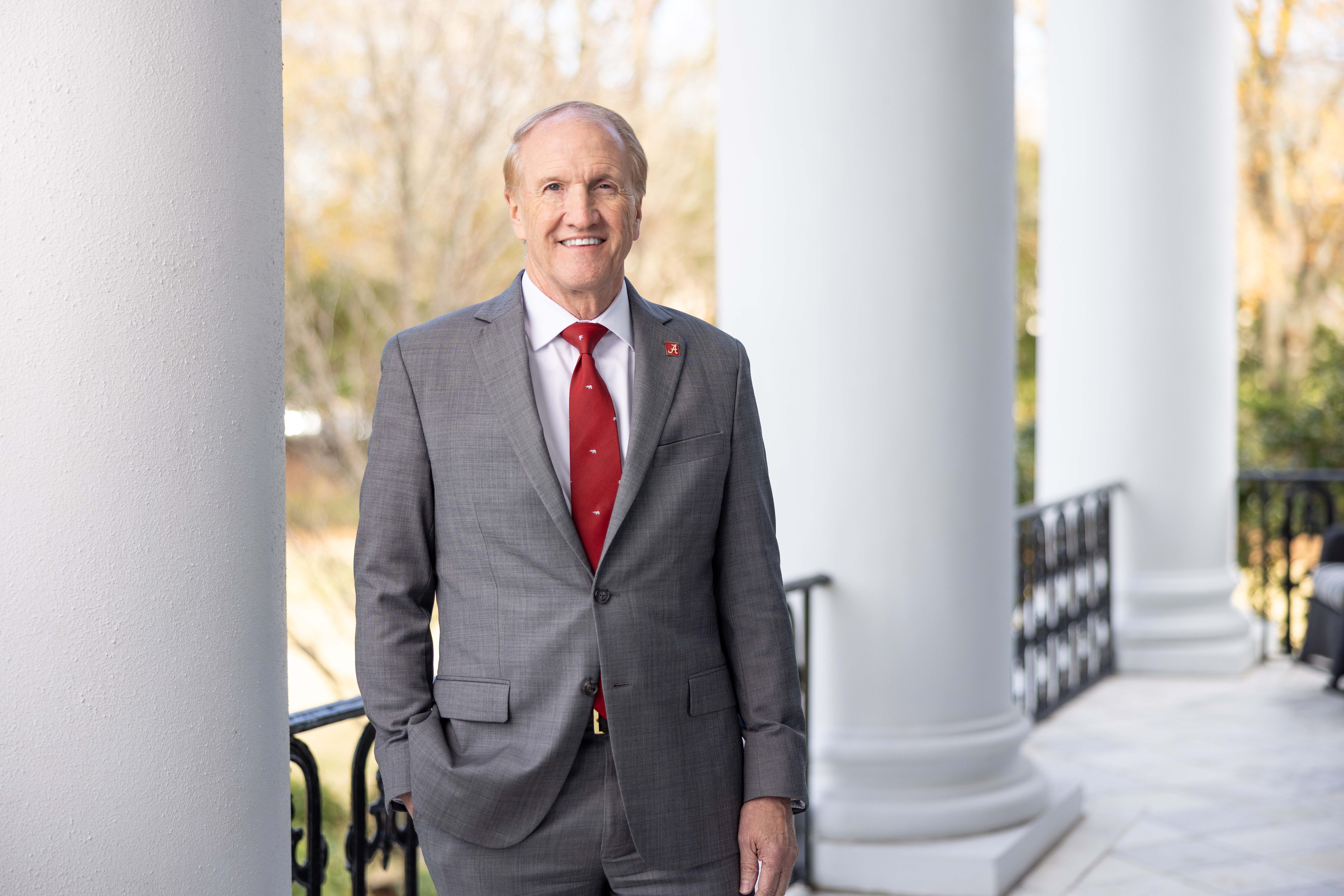 A white male stands on a porch near columns and poses for a photo