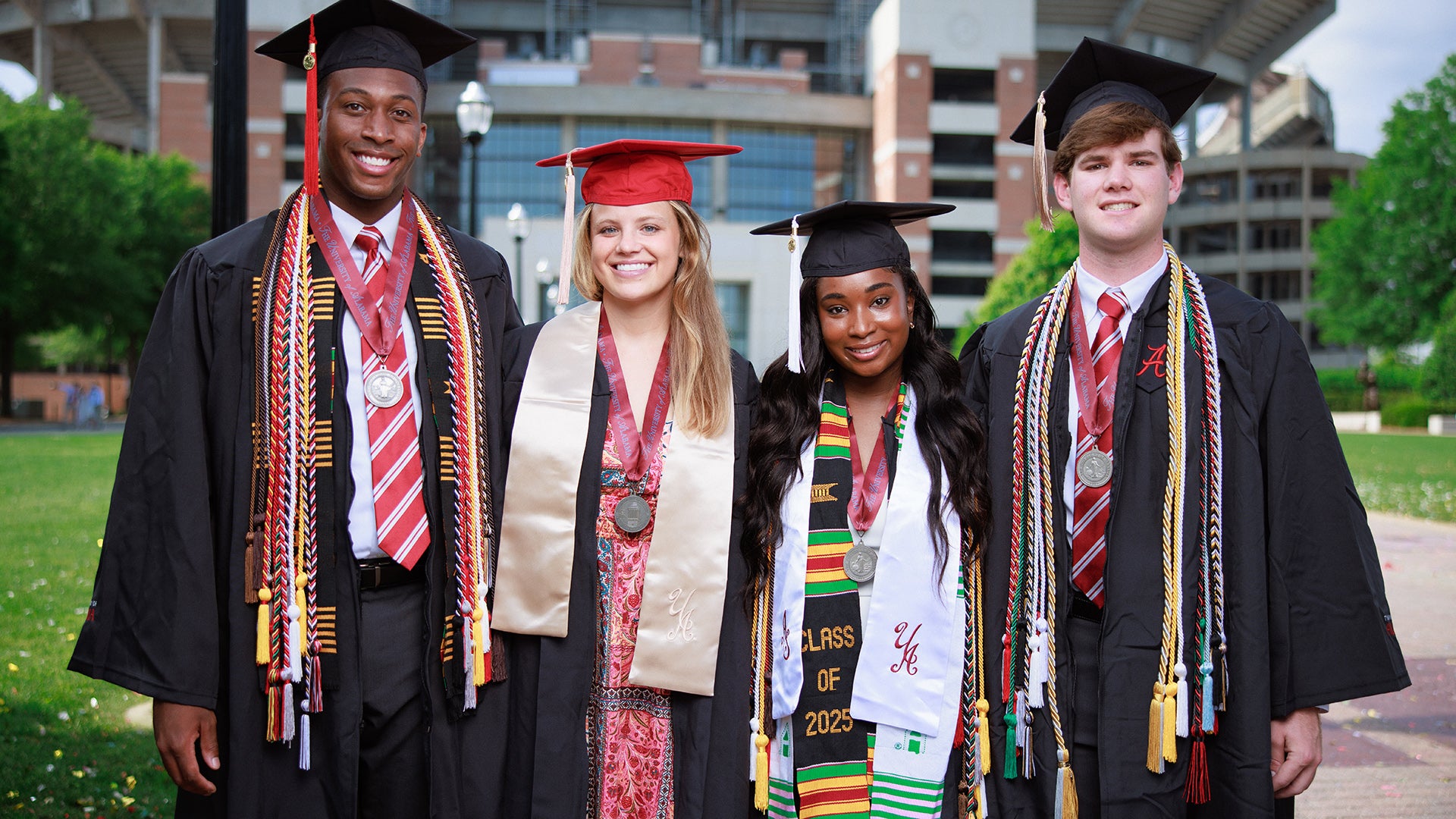 Two men and two women pose for a photo while wearing graduation regalia