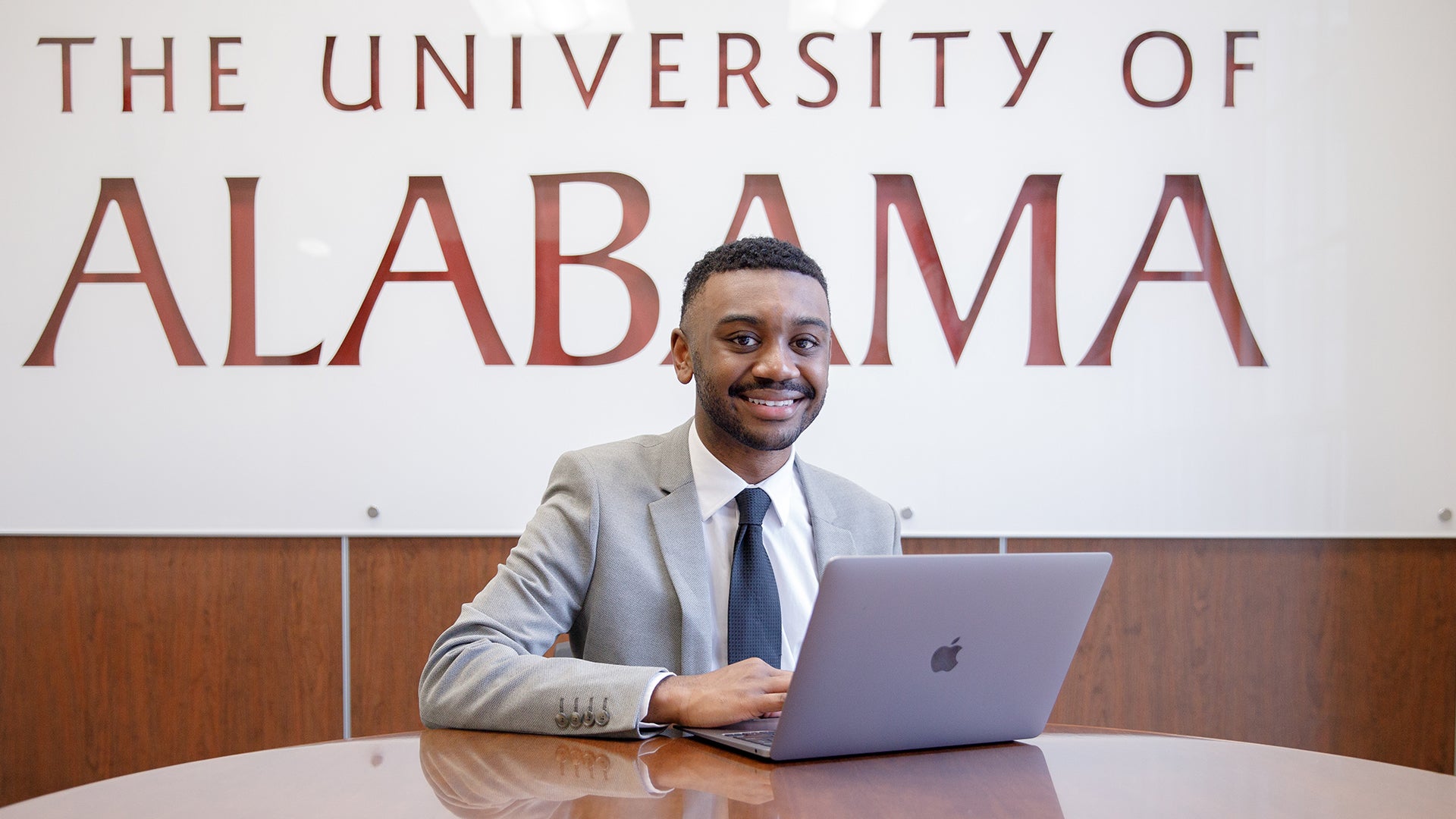 A male college student sits at a table with a laptop computer