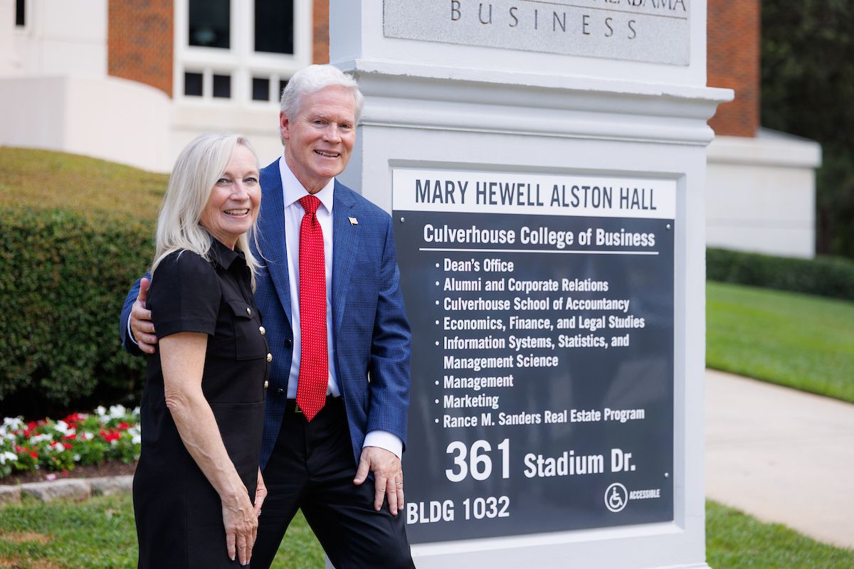 A man and a woman pose for a photo next to a sign.