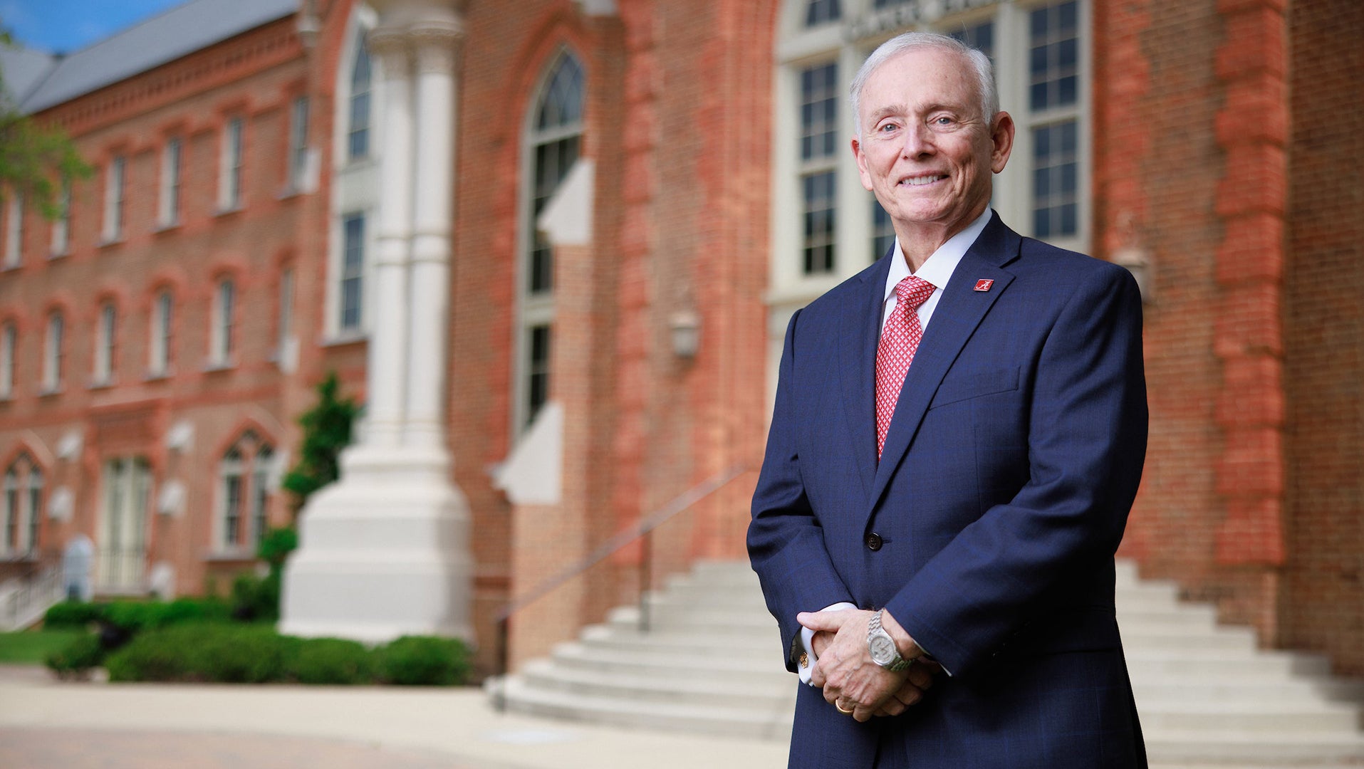 A man poses for a picture while standing in front of a brick building on a college campus