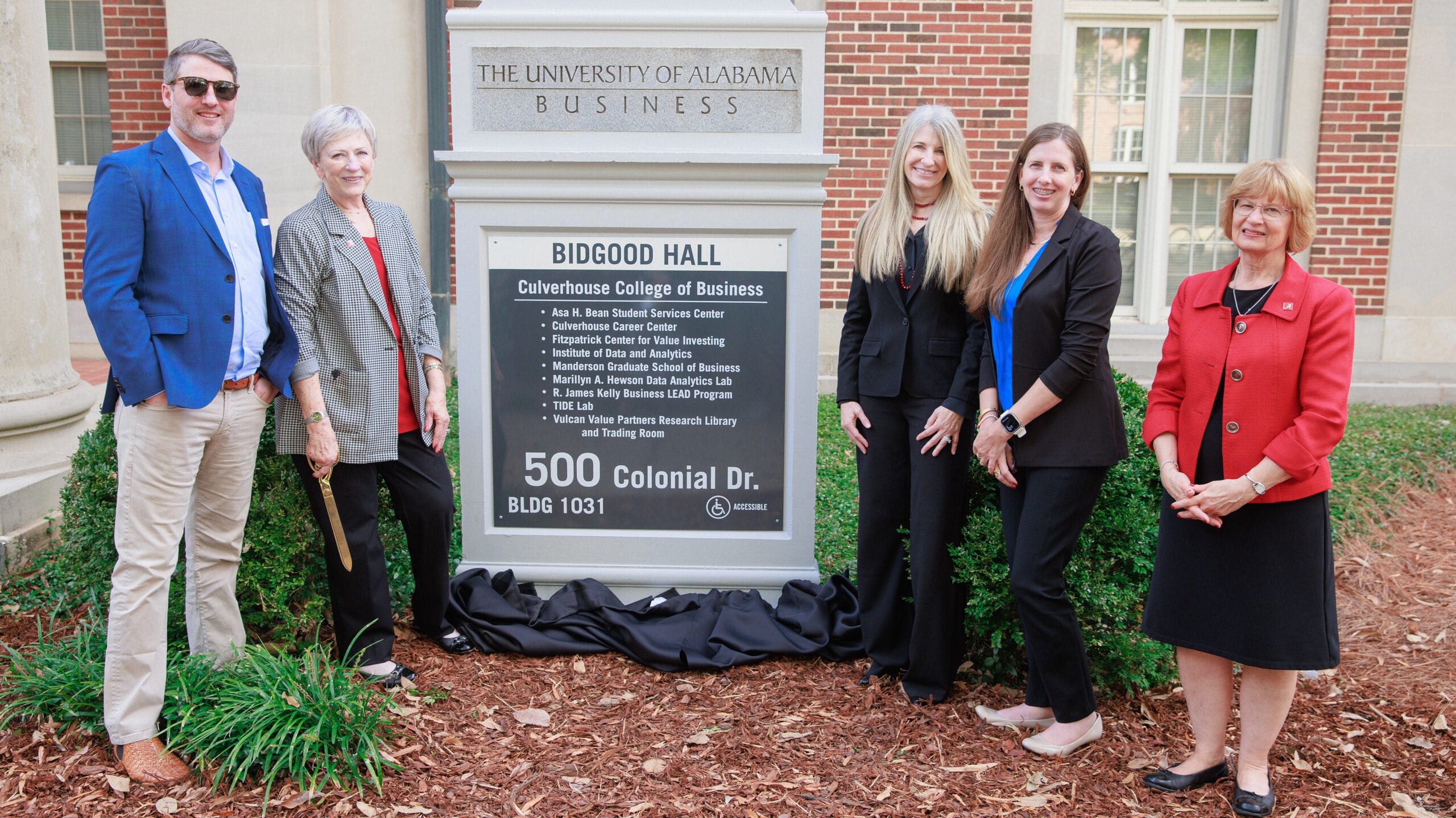 a man and four women stand next to a sign in front of a building