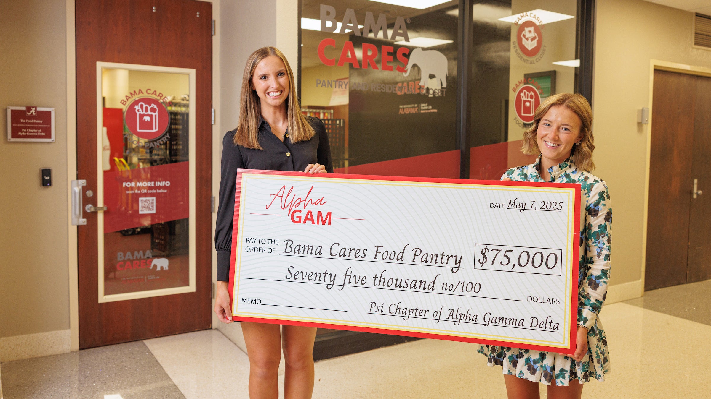 Two female college students hold an oversized check in front of a food pantry