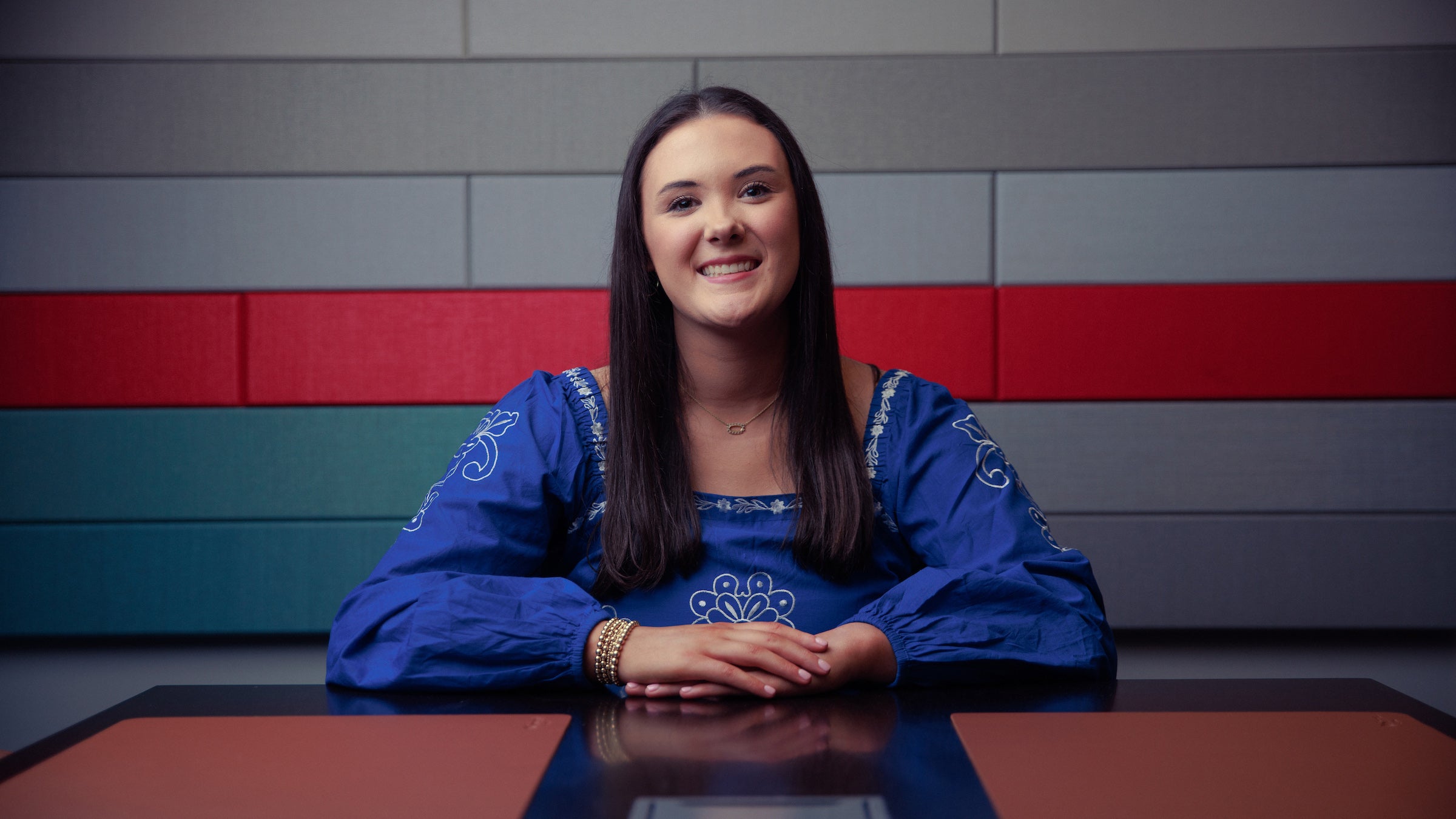 A female college student sits at a table and poses for a photo