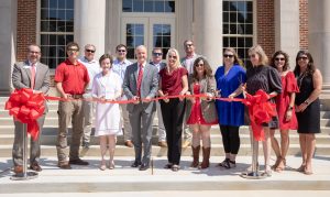 A group of people cut a ribbon to celebrate the opening of a building on a college campus