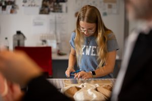 A white female student measures a garment in a design studio