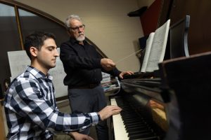 A white man teaches piano to a white college student