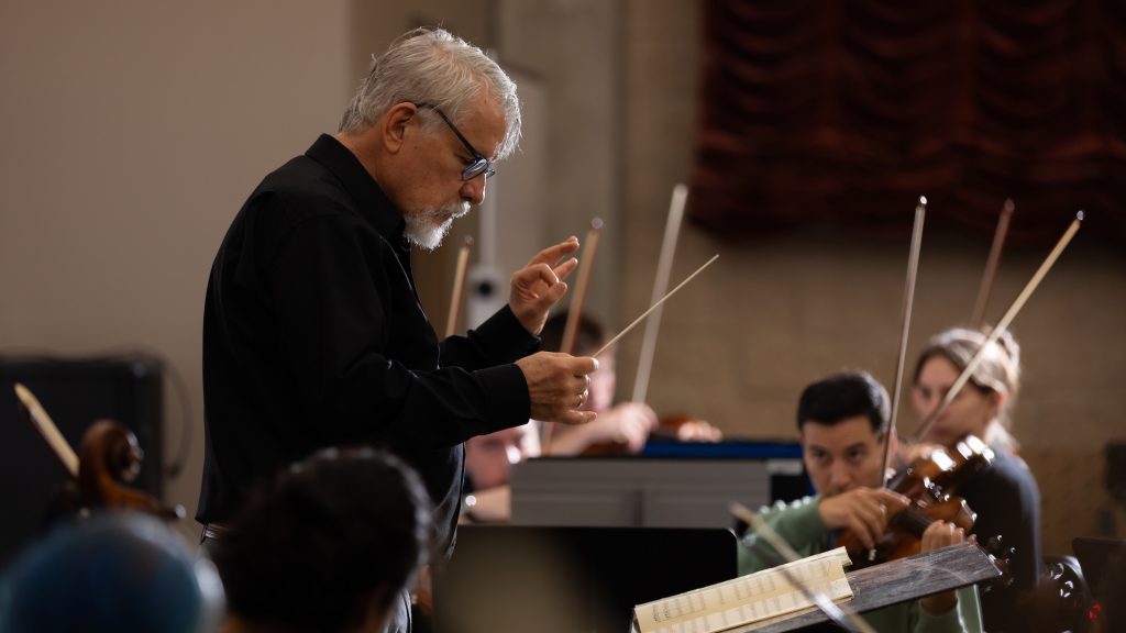 A white male conducts an orchestra