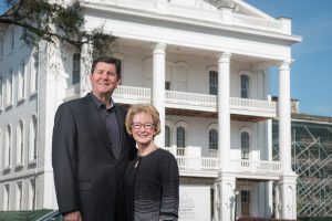 A man and woman pose for a photo outdoors in front of a white building