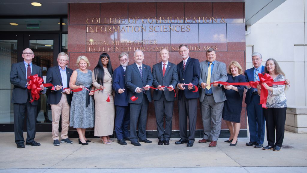 A group of people cut a large ribbon in front of a building